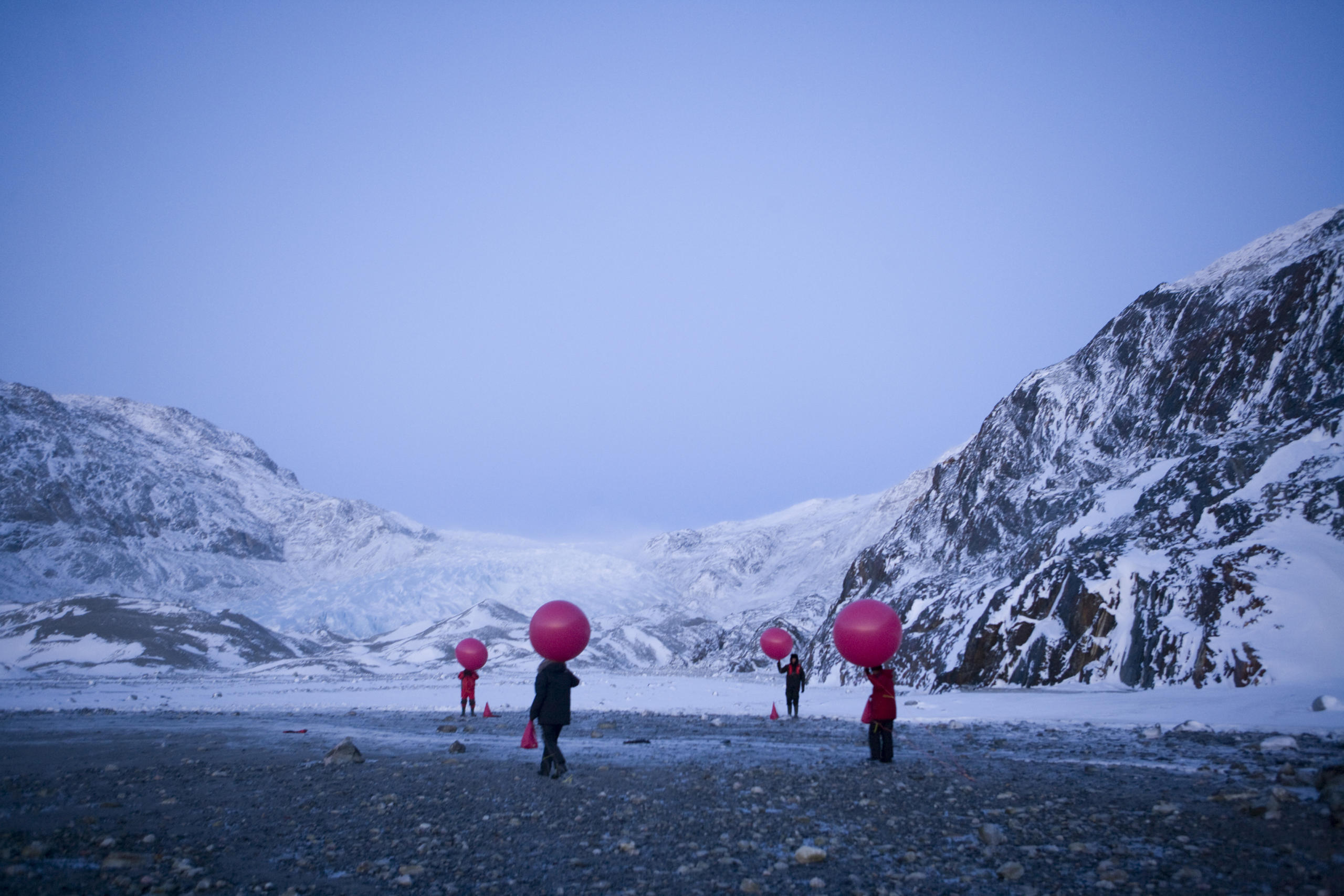figures holding red weather balloons in Arctic landscape