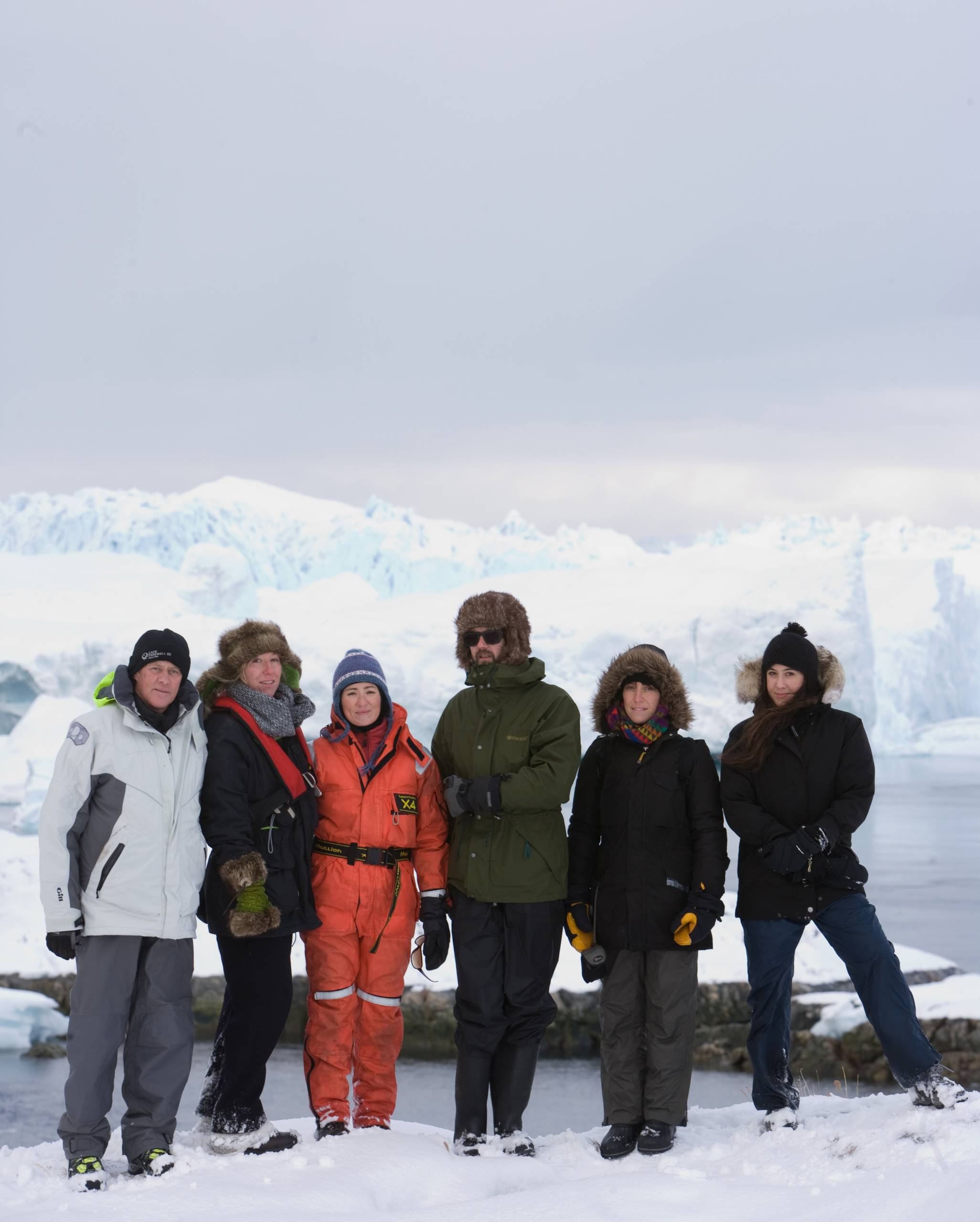 group in Arctic clothing gather in front of a glacier