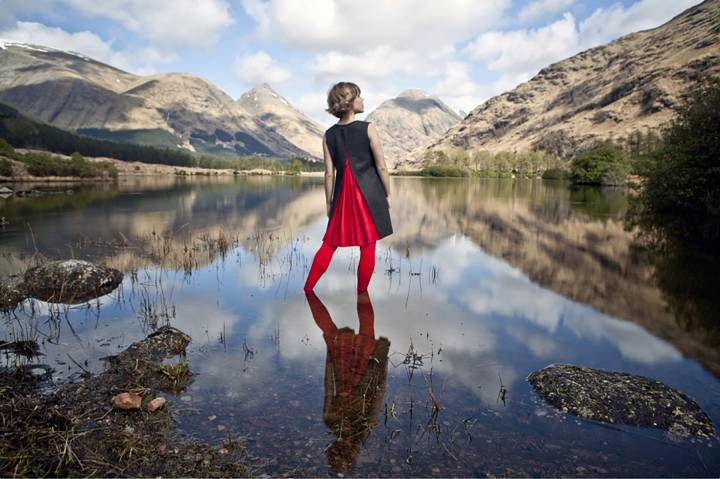 woman stands reflected in a vast lake landscape